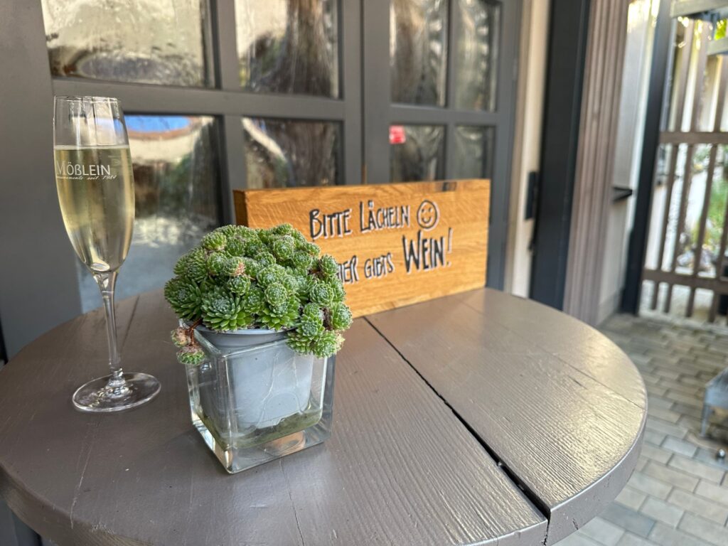 Sektglas und Holzschild "Bitte lächeln – hier gibts Wein!"