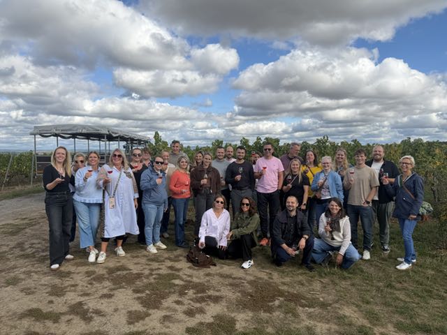 Gruppenfoto des Kollegiums im Weinberg vor Wolkenhimmel