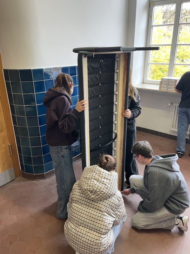 Schülerinnen und Schüler halten und schrauben gemeinsam ein größeres Möbelstück