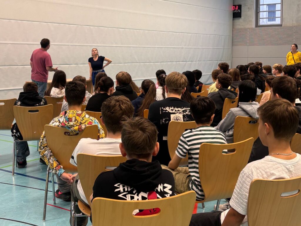 Schülerinnen und Schüler verfolgen in der Halle das Theaterstück